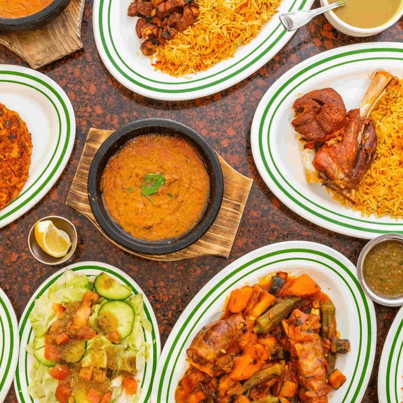 A table laden with various Middle Eastern dishes, including rice, meat, stews, and salad.