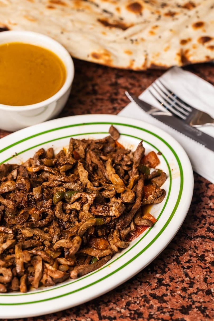 A plate of sautéed liver with vegetables, a bowl of soup, and flatbread on a marble table.