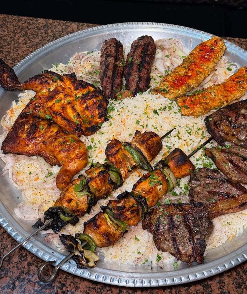 Large platter of grilled meats including chicken, kebabs, and lamb chops, served over rice.