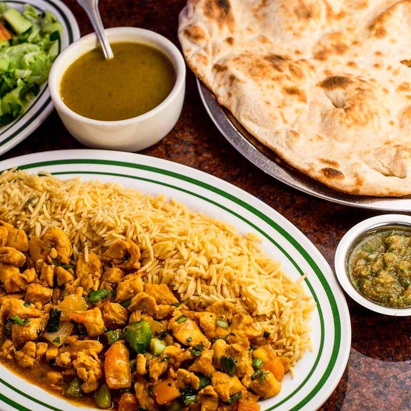 Chicken curry with rice, naan bread, green salad, and two dipping sauces on a table.