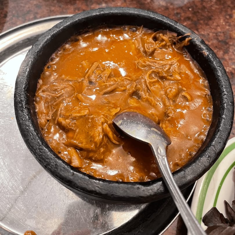 Close-up of a black bowl filled with a rich, orange-brown stew and a spoon.