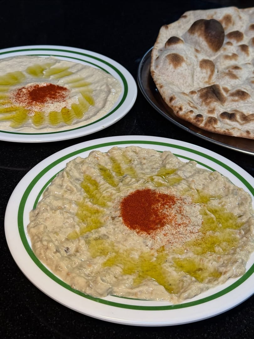 Two plates of hummus and baba ghanoush with olive oil and paprika, alongside flatbread.