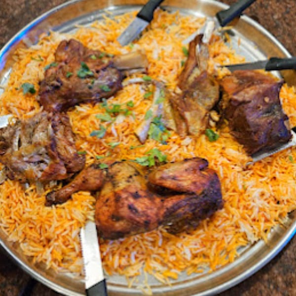 A large platter of Yemeni Mandi with roasted chicken and lamb pieces over saffron rice.