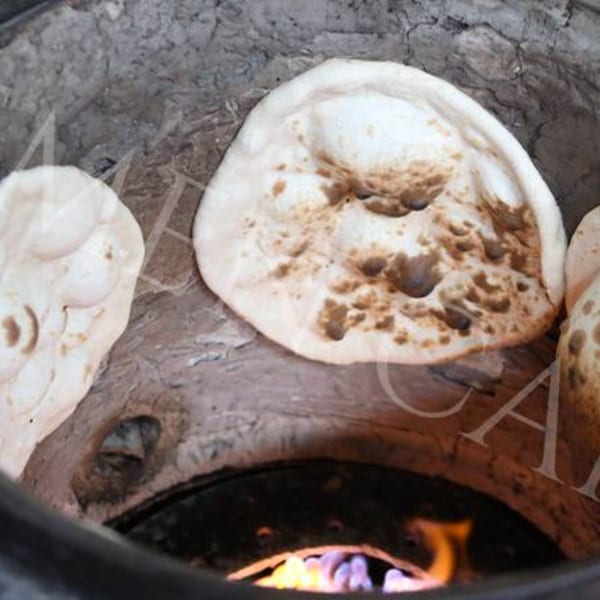 Freshly baked flatbreads cooking on the side of a traditional tandoor oven with flames visible below.