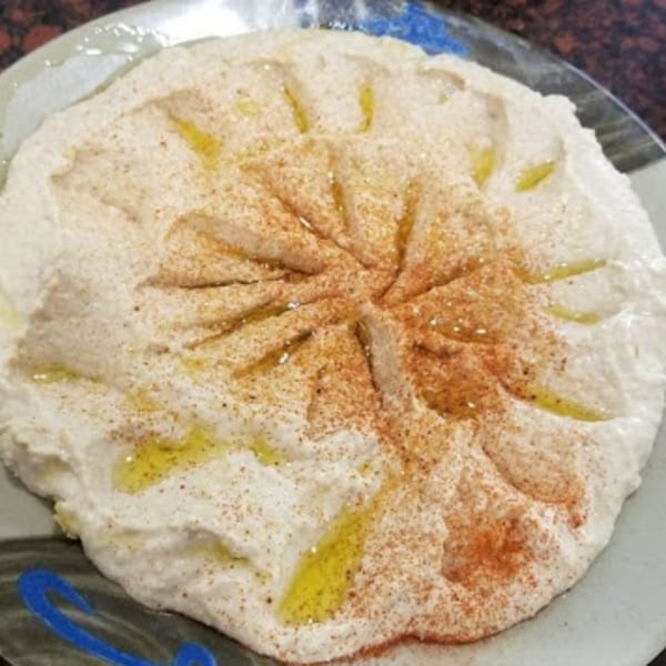 A plate of creamy hummus, drizzled with olive oil and sprinkled with paprika.