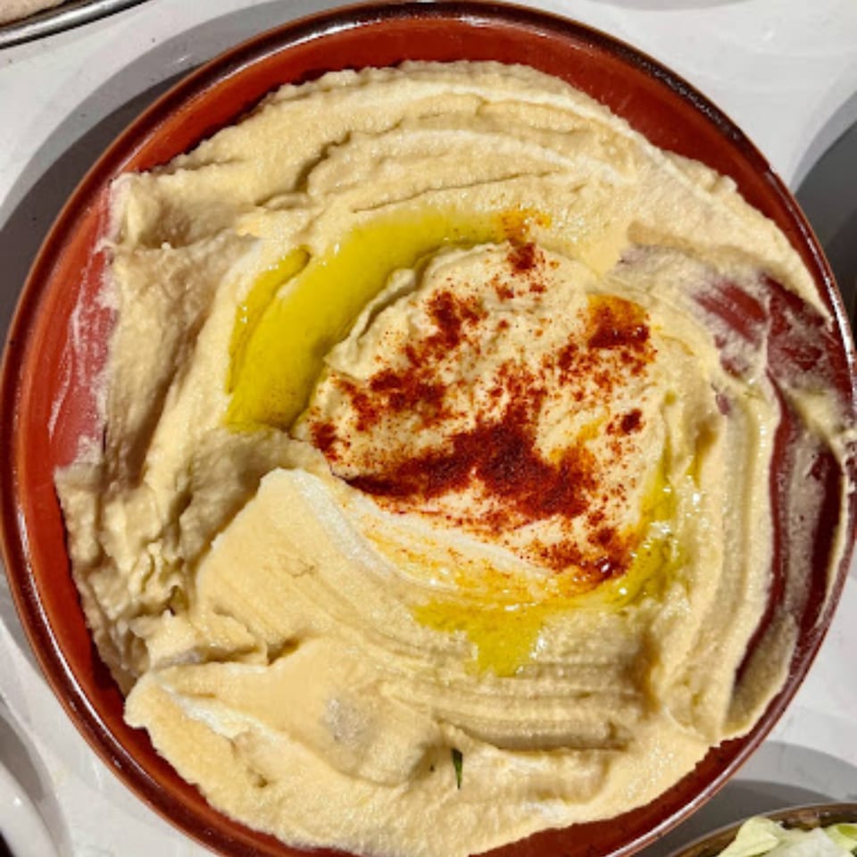 Creamy hummus in a brown bowl, drizzled with olive oil and sprinkled with paprika.