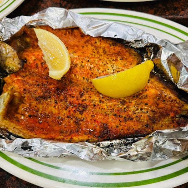 A large, seasoned fish fillet with two lemon wedges, served in foil on a white plate.