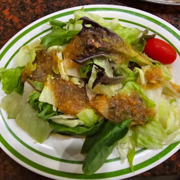 Fresh green salad with mixed lettuce, a single red grape tomato, and a savory dressing.