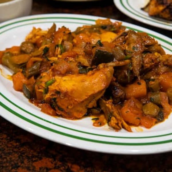 A close-up of a white plate with green stripes, filled with a hearty Middle Eastern stew.