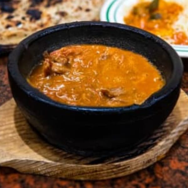 A black bowl of orange stew with meat, served on a wooden trivet at Yemen Cafe.