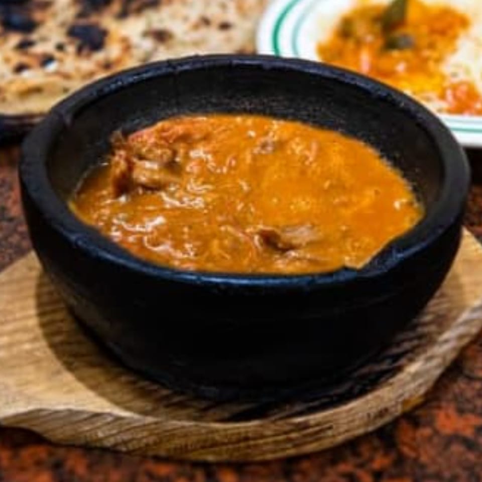 A black bowl of orange stew with meat, served on a wooden trivet at Yemen Cafe.