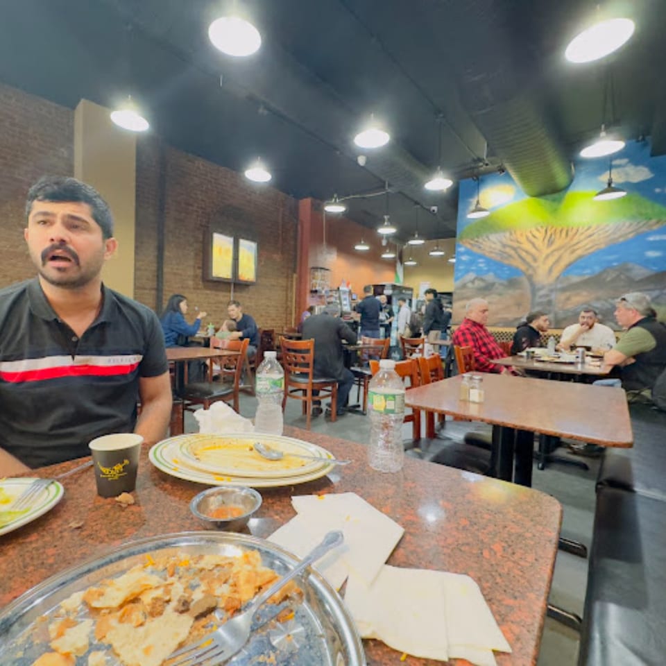 Diners enjoying Middle Eastern food at Yemen Cafe & Restaurant, with a man in the foreground.