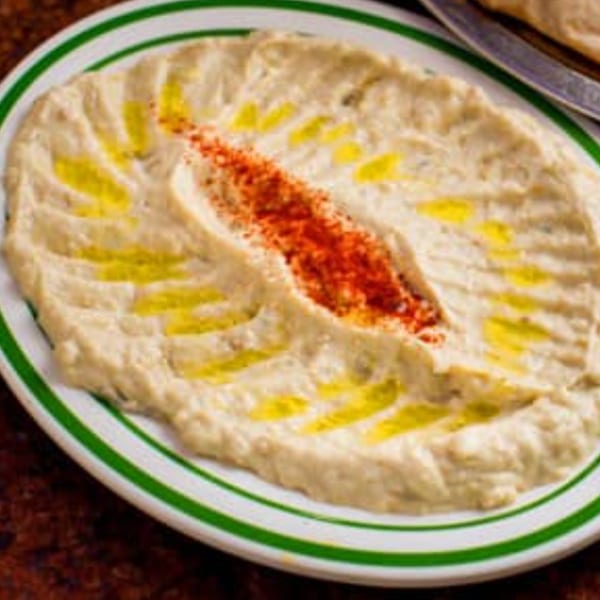 Creamy hummus with olive oil and a sprinkle of red paprika on a white plate with green stripes.