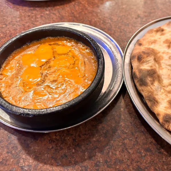 A close-up of a bubbling orange stew in a black bowl next to a piece of flatbread.