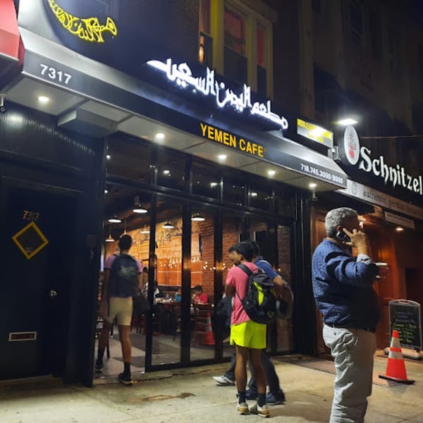Exterior of Yemen Cafe & Restaurant at night, with glowing signs and people entering the establishment.