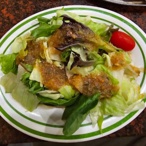 A fresh side salad with mixed greens, dressing, and a single cherry tomato on a white plate.