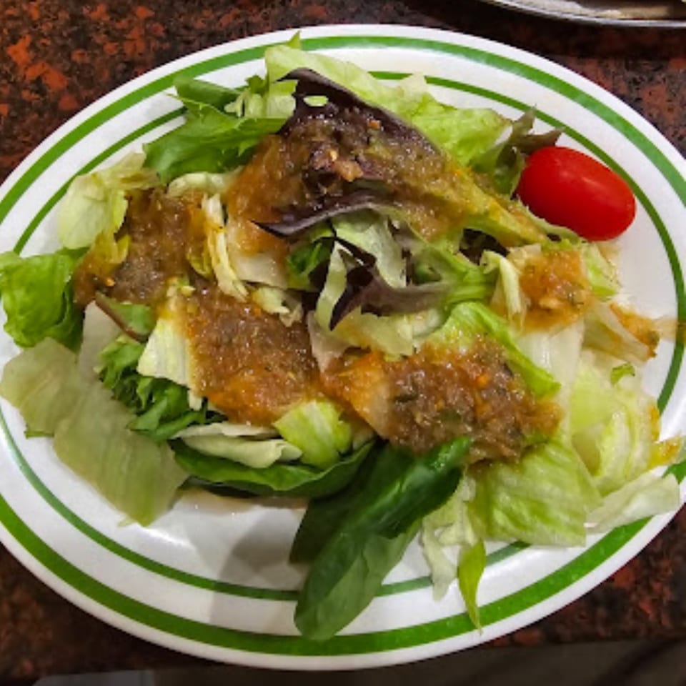 A fresh side salad with mixed greens, dressing, and a single cherry tomato on a white plate.