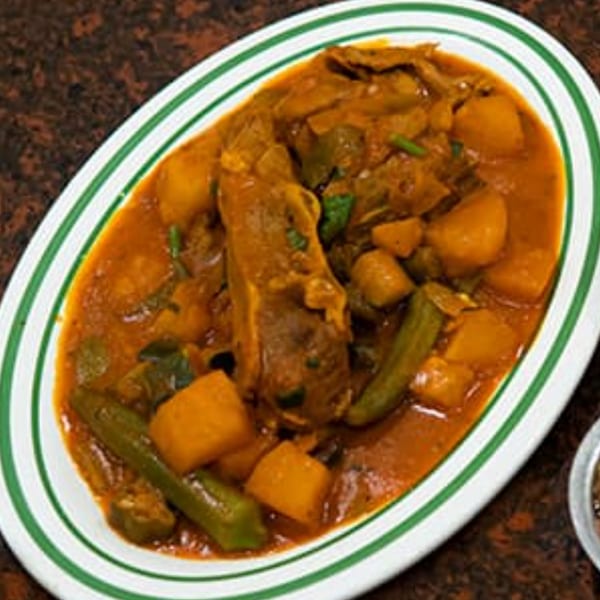 Hearty Yemeni stew with meat, potatoes, and okra in a rich red sauce, served on a white plate.