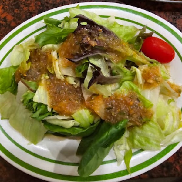 A fresh green salad with mixed greens, a single cherry tomato, and a savory dressing.