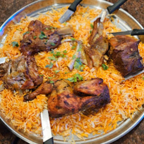 Large platter of Middle Eastern mandi rice with roasted chicken and lamb, garnished with parsley.