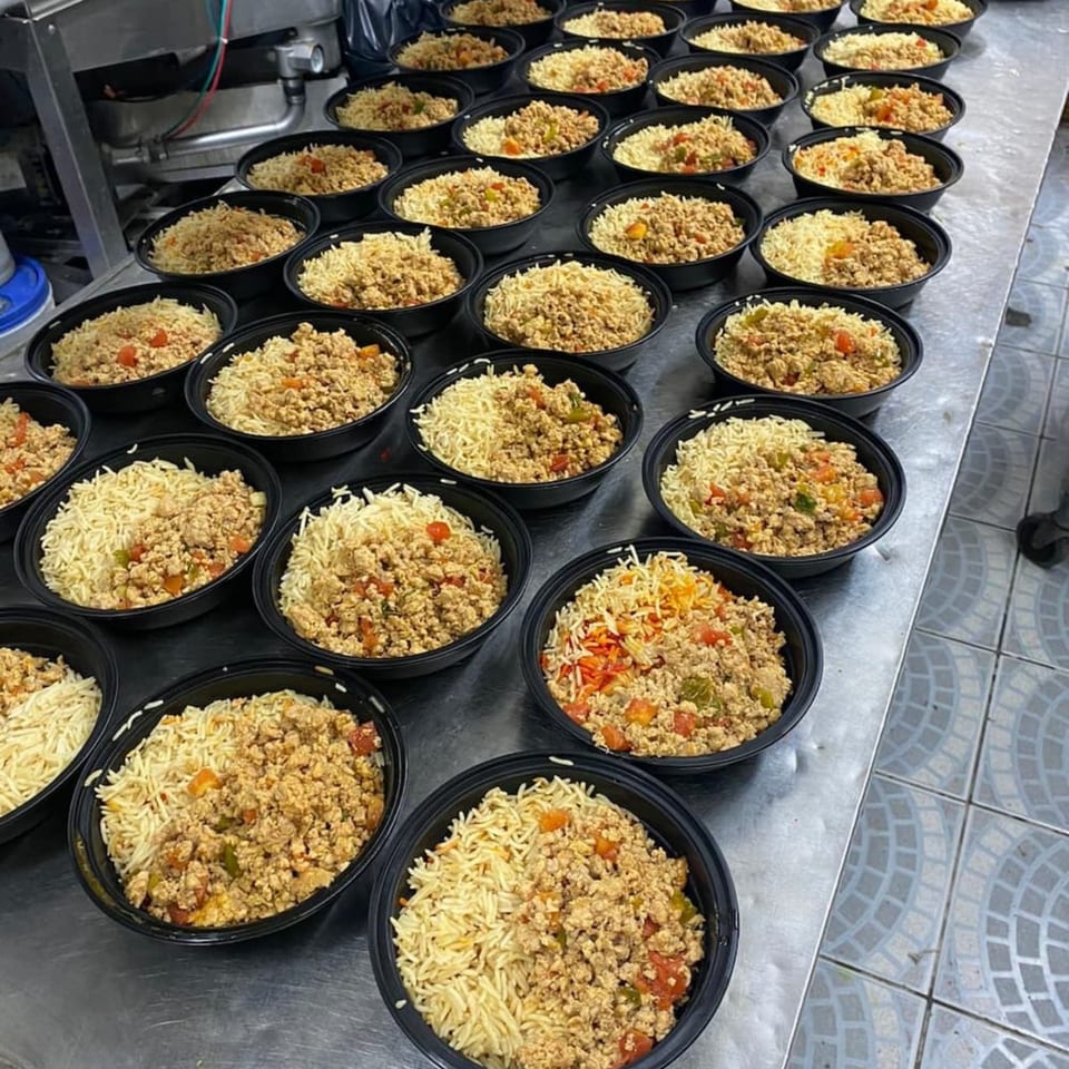 Rows of black bowls filled with Yemeni rice and seasoned ground meat on a metal counter.