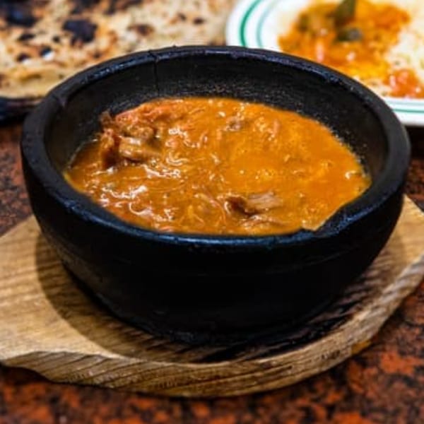 A black bowl of orange stew with meat, served on a wooden board at Yemen Cafe.