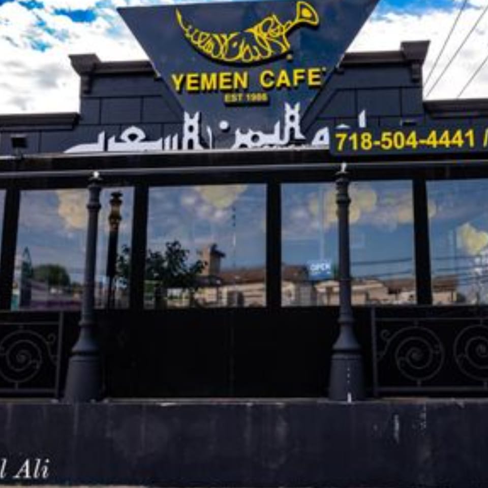 Exterior of Yemen Cafe & Restaurant, a black building with large windows and yellow signage.