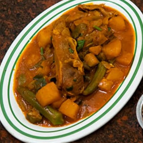 A white oval plate with green stripes holds a hearty stew of meat, potatoes, and okra in a rich orange sauce.